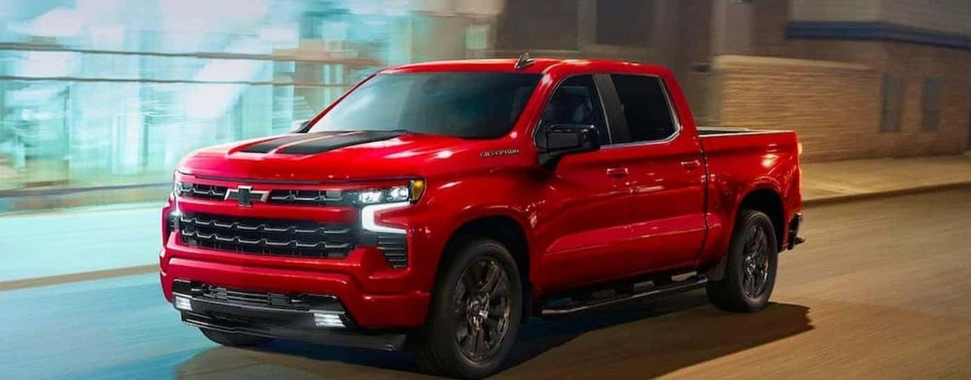 A red 2023 Chevy Silverado 1500 RST is shown driving on a city street.