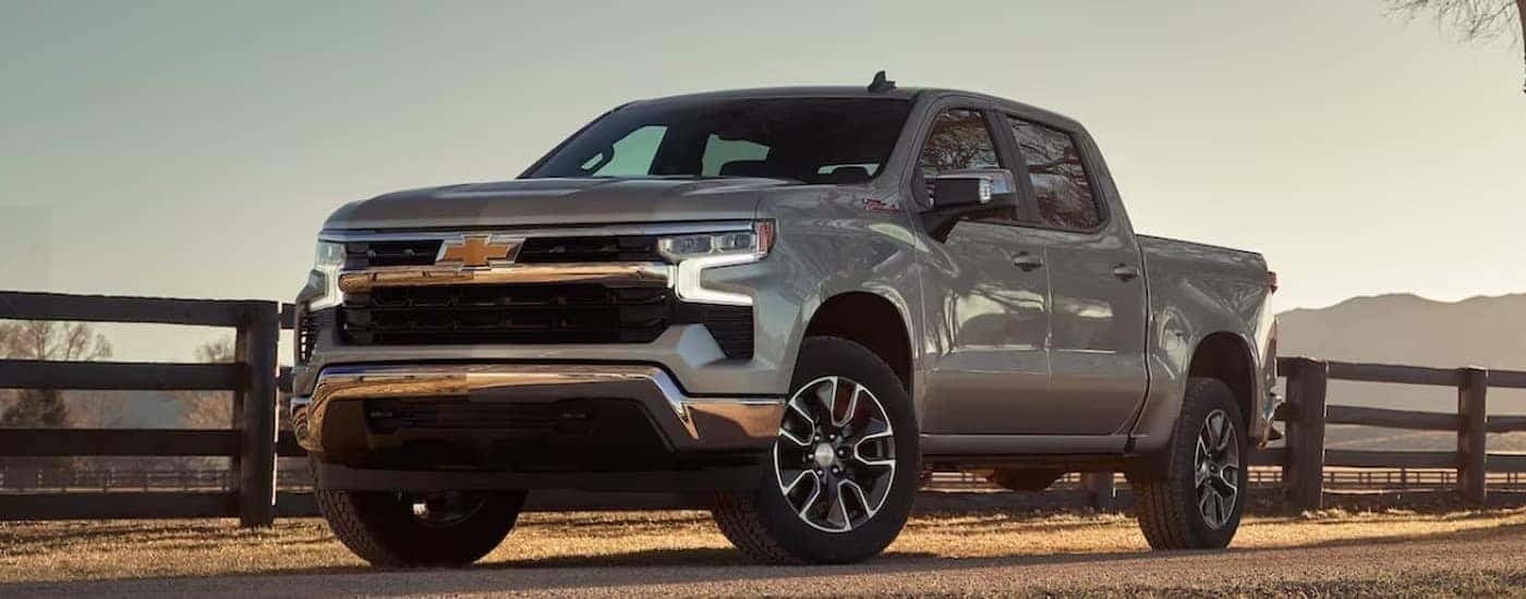 A silver 2024 Chevy Silverado LT Z71 is shown parked next to a wooden fence.