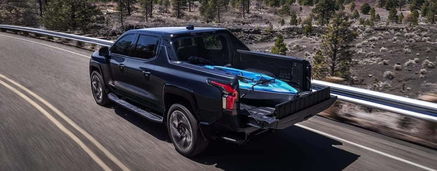 A black 2024 Chevy Silverado Ev is shown driving on a highway.
