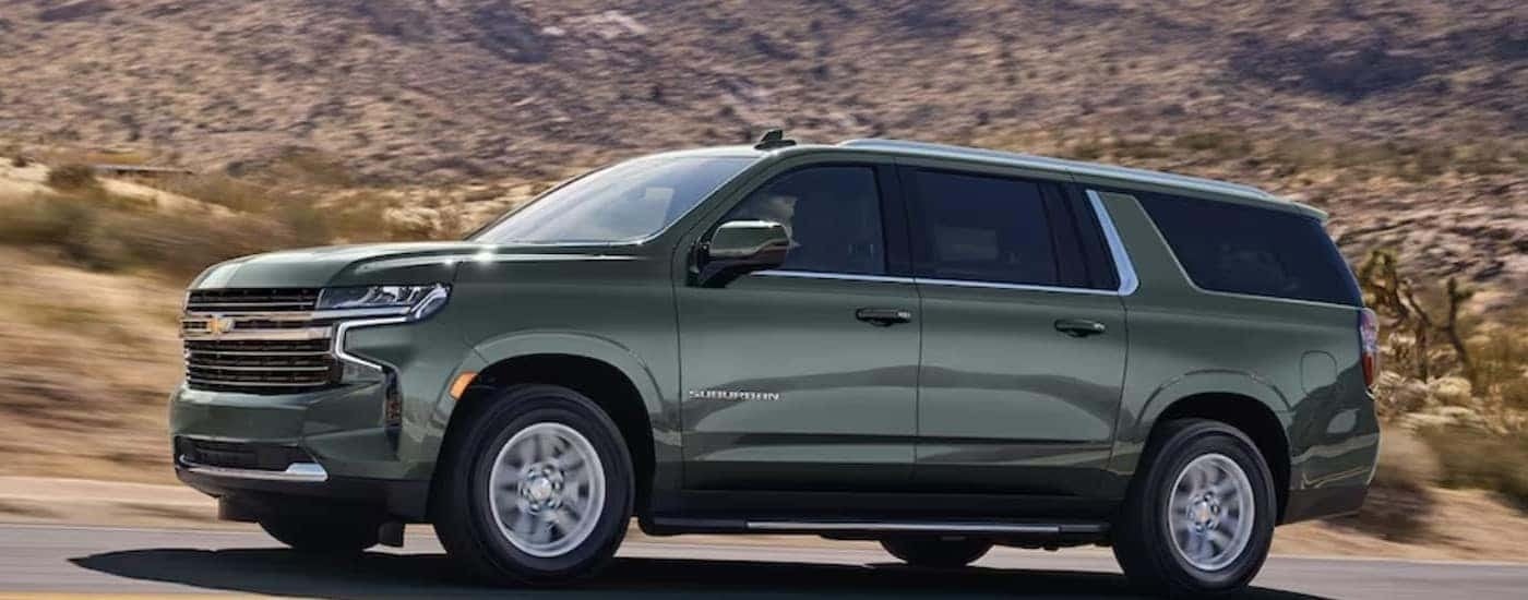 A green 2024 Chevy Suburban is shown driving on a highway.