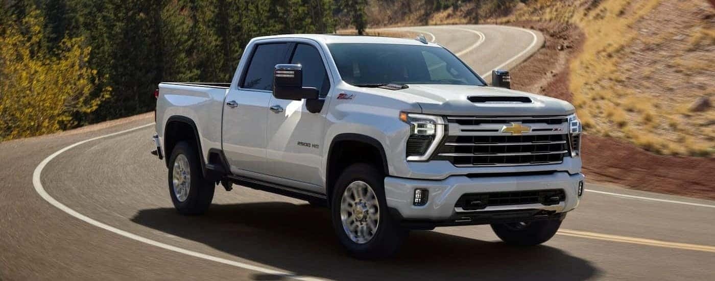 A white 2025 Chevy Silverado 2500 HD Z71 is shown driving on a highway.