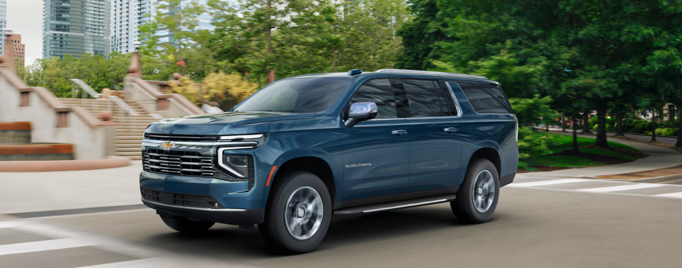 A blue 2025 Chevy Suburban driving down the road after leaving a Chevy dealer near Chelsea