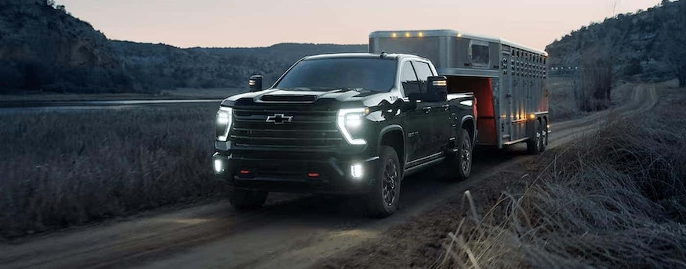 Black 2026 Chevy Silverado 2500HD towing a trailer on a dirt road