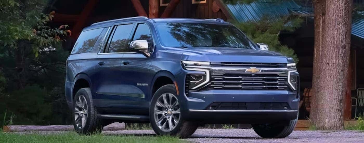 A blue 2025 Chevy Suburban is parked outside of a car dealer