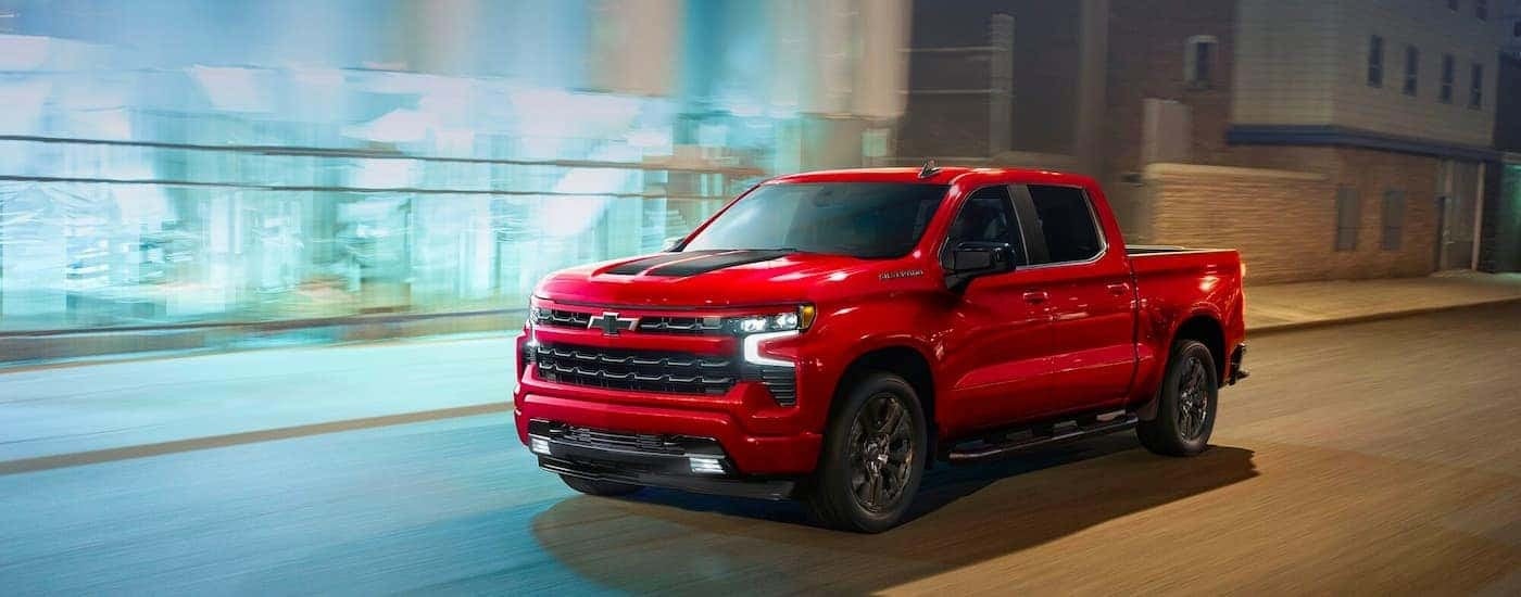 A red 2023 Chevy Silverado 1500 RST is shown driving on a city street at night