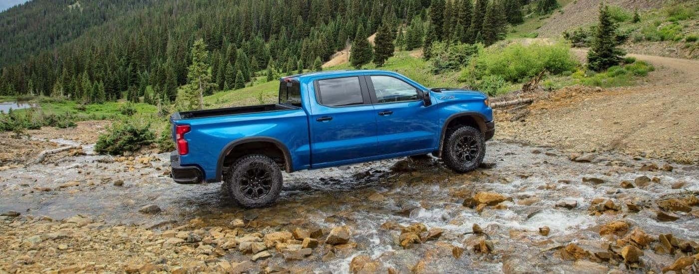 A blue 2026 Chevy Silverado ZR2 is shown driving through a creek