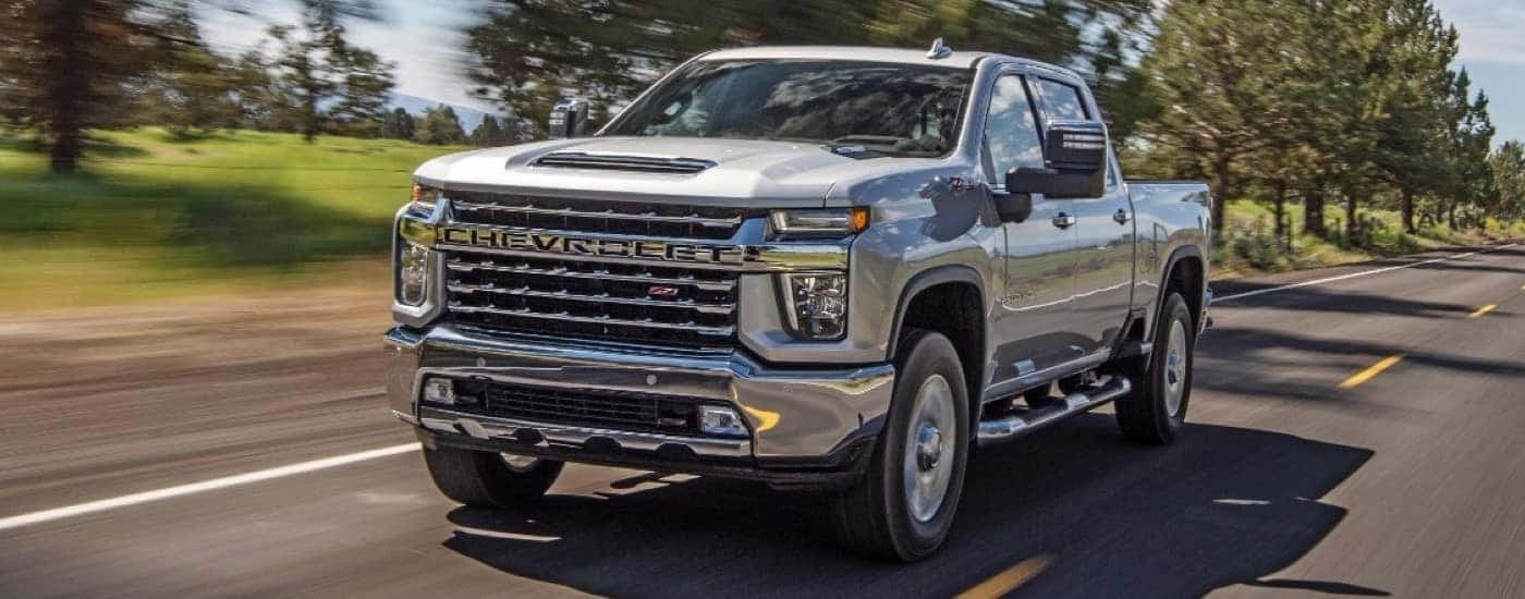 A silver 2021 Chevy Silverado 2500HD, a popular used Chevy truck for sale, is shown driving down an open road.